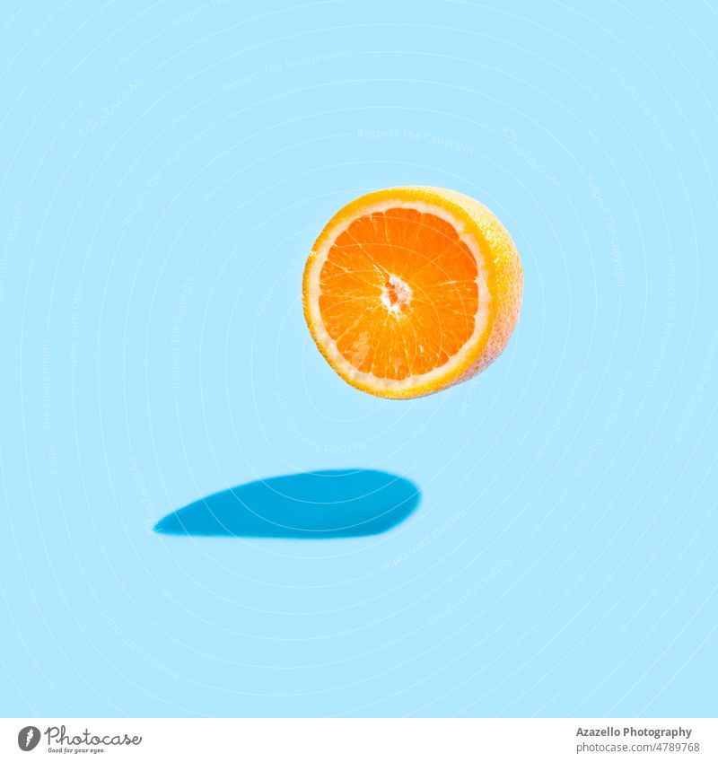 Isolierte orangefarbene Hälfte mit einem echten Schatten auf blauem Hintergrund. Fliegende Orange auf Blau. Minimalismus Stillleben Entgiftung gesunde Ernährung