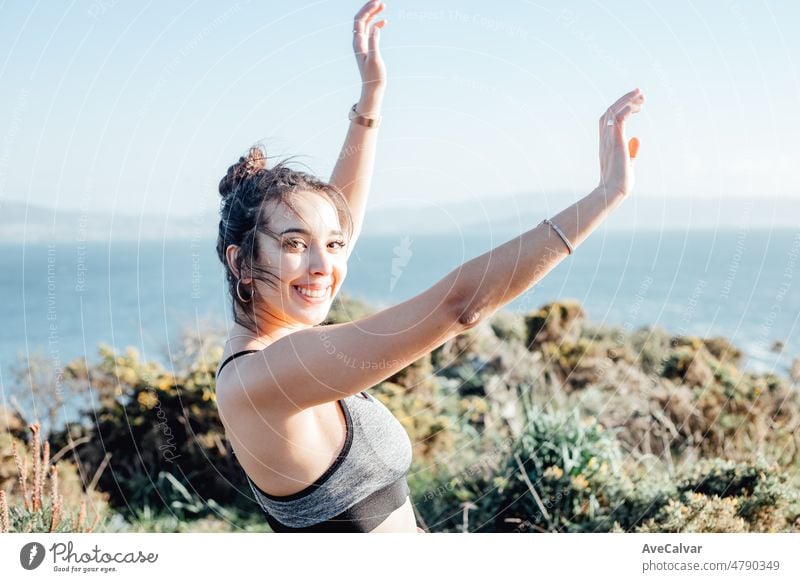 Junge Frau feiert den Abschluss einer Trainingseinheit im Freien an der Küste. Sie tanzt und reckt die Arme in die Luft. Glückliche junge Leute trainieren an einem sonnigen Sommertag und bereiten sich auf den Strandkörper vor