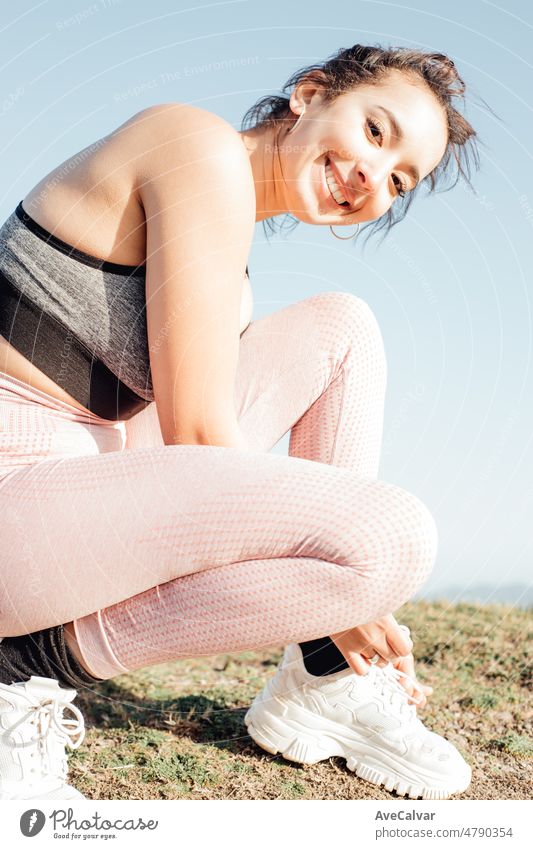 Junge Frau schnürt ihre Schuhe und lächelt in die Kamera. Glückliche junge Menschen, die an einem sonnigen Sommertag trainieren und sich auf den Strandkörper vorbereiten. Training Kleidung.