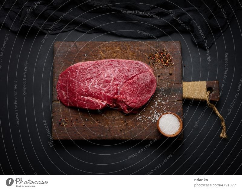 Rohe Rinderlende liegt auf einem Schneidebrett und Gewürzen zum Kochen auf einem schwarzen Tisch, Ansicht von oben Vorbereitung Transparente Rindfleisch