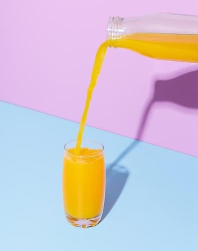 Orangensaftglas auf einem blauen Tisch. Einschenken von Orangensaft. Hintergrund Getränk Flasche Frühstück hell Zitrusfrüchte Nahaufnahme Farbe farbenfroh zyan