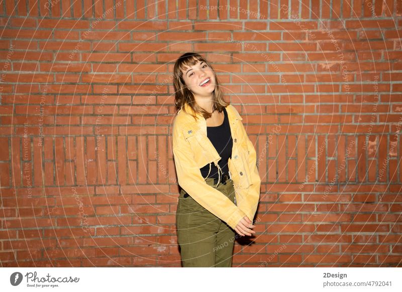 Junge Frau steht in der Nähe einer alten Backsteinmauer in der Stadt bei Nacht jung Stehen attraktiv Lächeln Glück Wand Baustein Freizeitkleidung Person schön