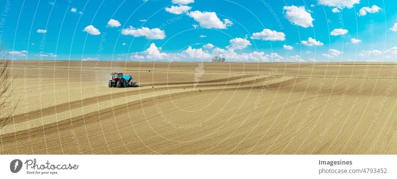 Ackerbau. Landwirt mit Traktor, der Getreide auf dem Feld sät. blauer traktor mit egge auf dem feld vor bewölktem himmel, landmaschinenarbeit. Land für die Aussaat vorbereiten