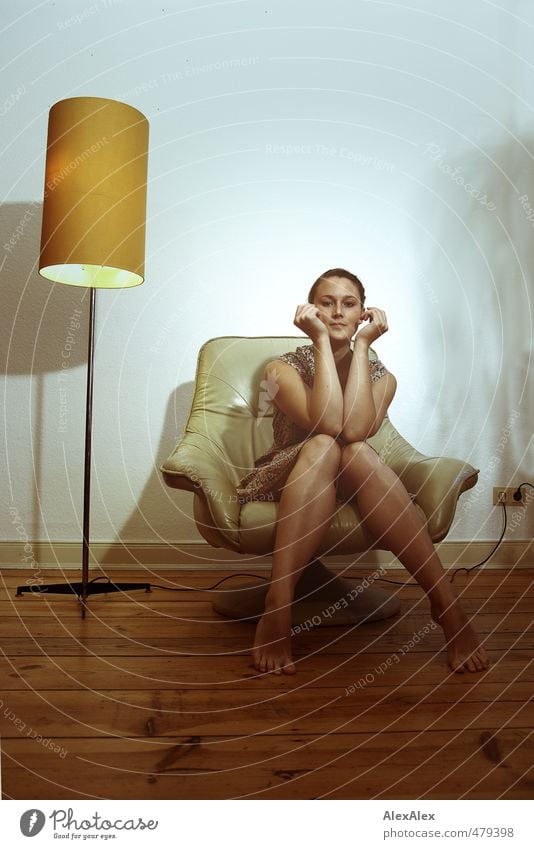 Junge Frau in Kleid sitzt barfuß auf einem Sessel und hält die Arme zum Gesicht Stehlampe Jugendliche Beine Gesichtsausdruck 18-30 Jahre Erwachsene Sommerkleid