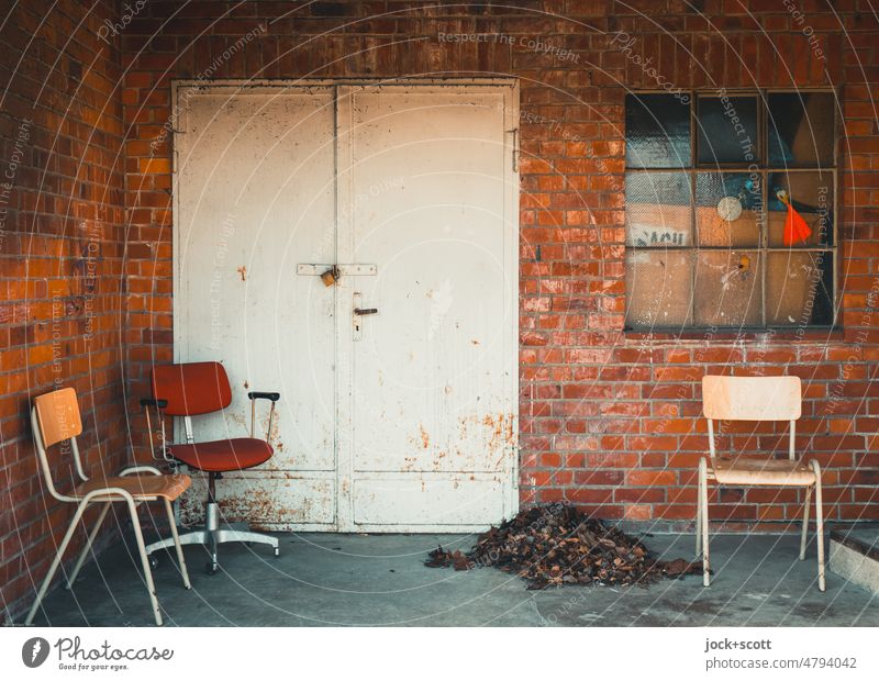 wartende Stühle neben einem Laubhaufen Stuhl Sitzgelegenheit Platz Pause Fenster Metalltür Menschenleer frei klinker Fensterkreuz Pausenplatz Ecke abgestellt