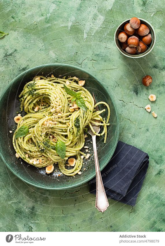 Keramikteller mit Haselnuss-Pesto-Spaghetti auf grüner Tischoberfläche Schalen & Schüsseln rustikal Abendessen kulinarisch Basilikumblätter Serviette