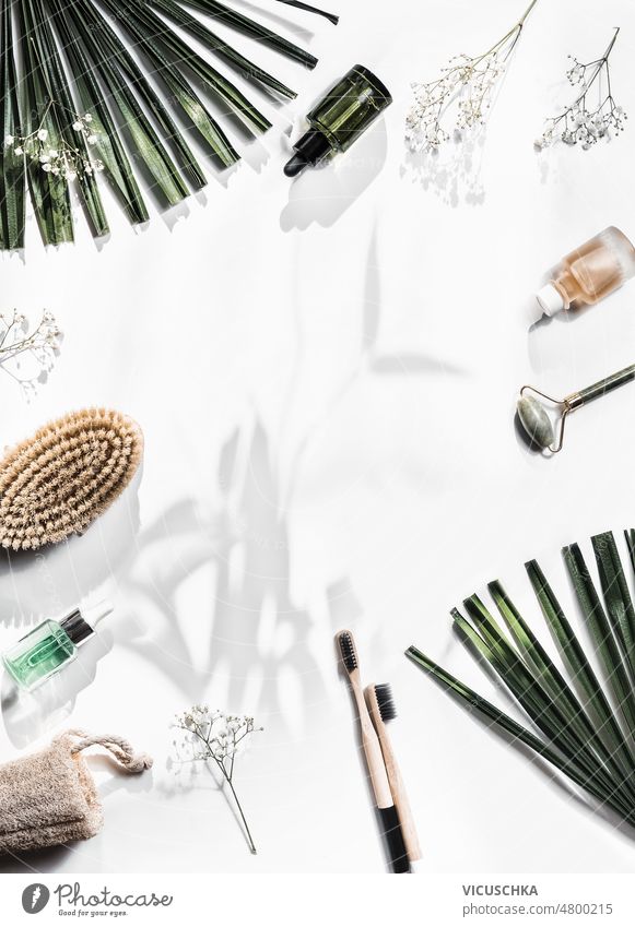 Nachhaltige Schönheit Hintergrund mit Massage-Bürsten, Bambus-Zahnbürsten, Kosmetik-Flaschen, Jade Roller und Schwamm auf weißem Hintergrund mit Palmenblättern