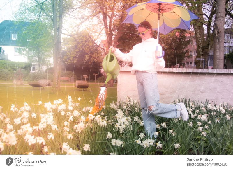 Mädchen mit Sonnenschirm steht im Blumenbeet und giesst die Blumen Frühling Giesskanne Garten Gartenarbeit Wasser gießen Außenaufnahme Pflanze Gärtner Natur