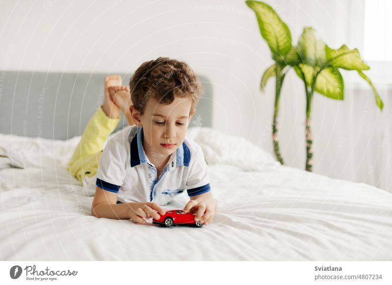 Ein kleiner Junge liegt auf dem Bauch und spielt mit einem Spielzeugauto auf seinem Bett PKW wenig Spielen Spaß niedlich Kind jung heimwärts Kaukasier spielen