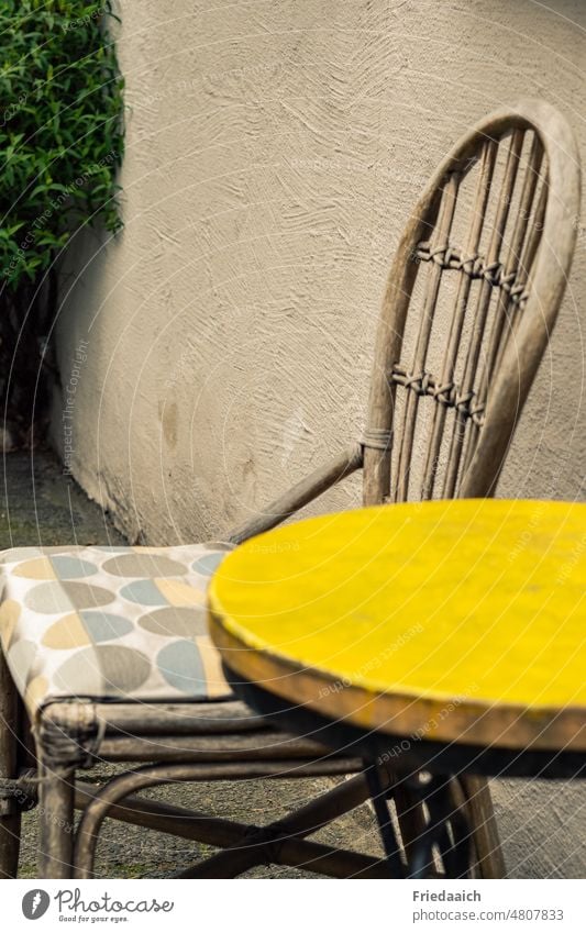 Holzstuhl und runder Tisch mit gelber Platte an einer Hauswand Stuhl sitzplatz Sitzecke gemütlich Außenaufnahme Farbfoto Sitzgelegenheit Möbel leer ruhig