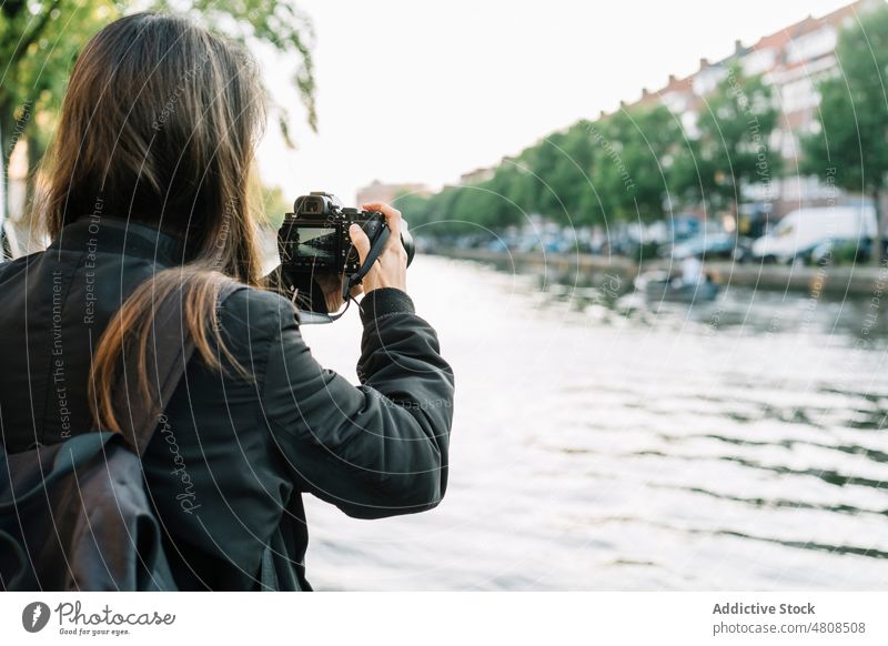 Fotografin fotografiert den Fluss vom Ufer aus in der Stadt Frau fotografieren Fotoapparat Kanal Gebäude Großstadt Sightseeing Reisender Stauanlage Urlaub
