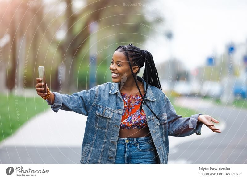 Junge Frau benutzt ihr Smartphone in der Stadt cool sorgenfrei selbstbewusst Tag Jahrtausende Rastalocken genießen authentisch positiv echte Menschen freudig