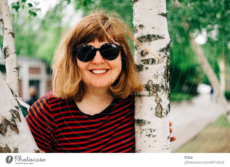[hansa BER 2022] Naturverbundene Frau strahlt mit weißer Birke um die Wette Baum Baumstamm Baumkuscheln weiblich lächeln gute Laune Frühling Sonnenbrille