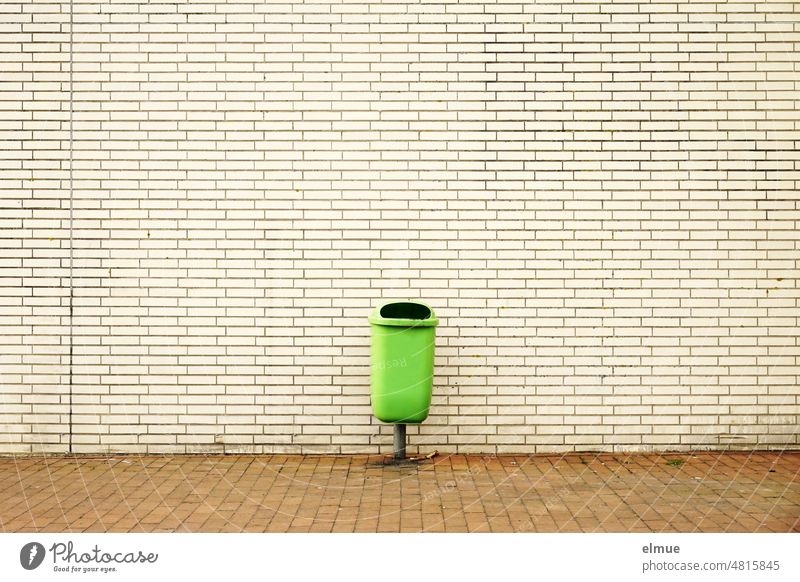 grüner Abfallbehälter für Restmüll vor einem Gebäude in beigefarbener Klinkerverkleidung / Müllentsorgung Außenabfallsammler Müllschlucker Papierkorb Stadtleben