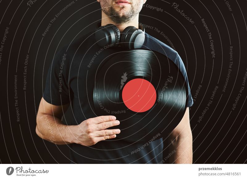 Mann hält Schallplatte über Herz. Leidenschaft für Musik. Vintage-Musik-Stil. Mann mit Kopfhörern, der eine alte Vinylplatte auf schwarzem Hintergrund hält. Retro-Musik