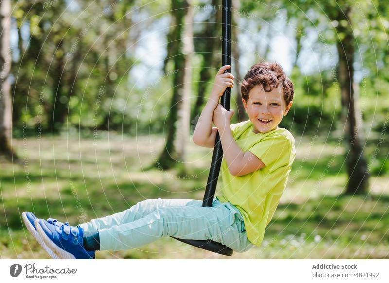 Fröhliches kleines Kind auf dem Schaukelseil auf dem Spielplatz lächelt in die Kamera pendeln Seil Lächeln Kindheit heiter Aktivität Junge Park positiv Porträt
