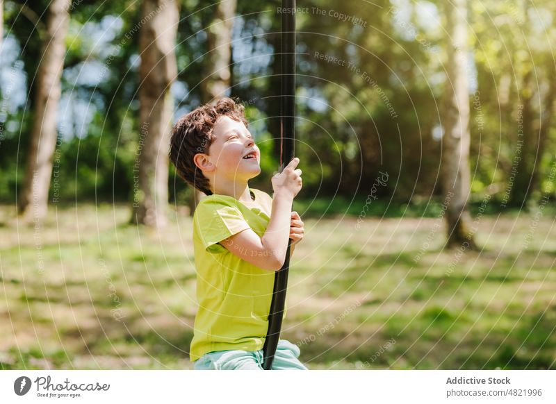 Fröhliches kleines Kind auf dem Schaukelseil auf dem Spielplatz lächelt vor sich hin pendeln Seil Lächeln Kindheit heiter Aktivität Junge Park positiv Porträt