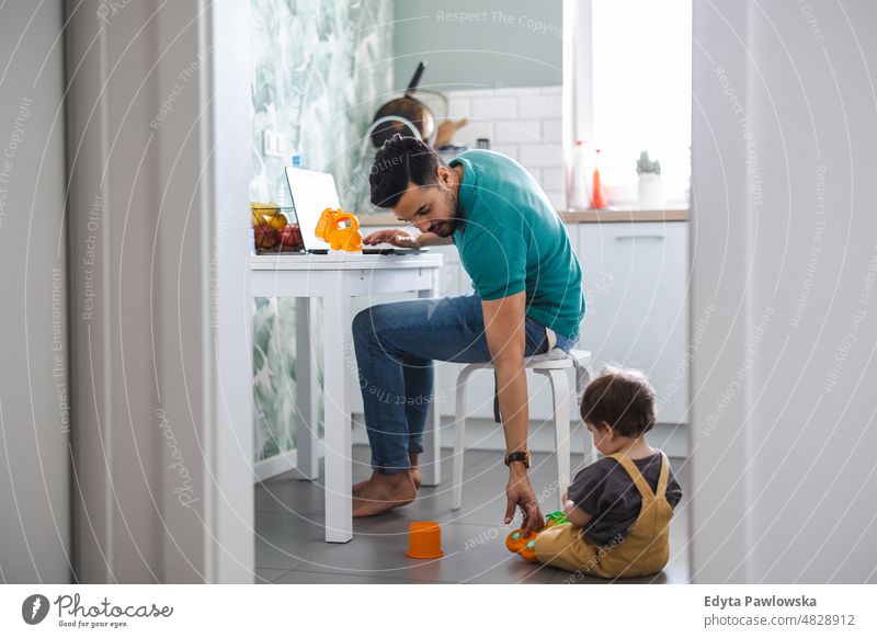 Vater arbeitet am Laptop, während das Kind auf dem Küchenboden spielt Erwachsener Zuneigung Baby Bonden Junge offen Pflege Kindheit heimisch genießend Familie