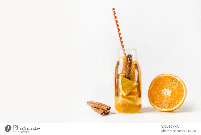 Leckere Limonade in einer Flasche mit Trinkhalm und Zutaten: Orange und Zimtstangen auf weißem Hintergrund. geschmackvoll orange weißer Hintergrund Sommer