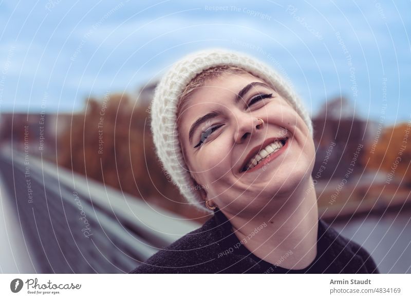 Porträt einer jungen Frau mit einer Mütze, die sehr glücklich ist Lächeln Glück Außenseite im Freien Brücke Fluss Herbst Himmel blau Teenager lässig Kaukasier