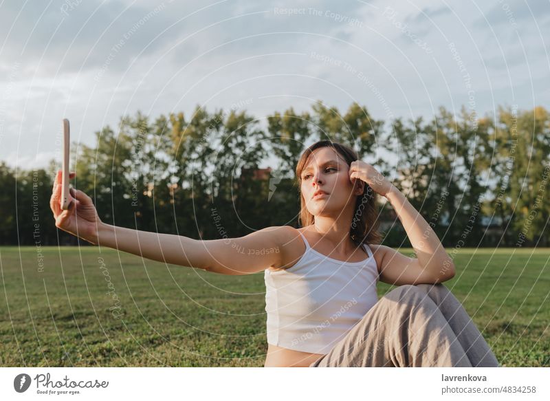 Junge Frau nimmt Selfie draußen während der goldenen Stunde Mädchen Porträt Natur aktiv Erwachsener brünett heiter Apparatur Gras Glück Gesundheit Lifestyle