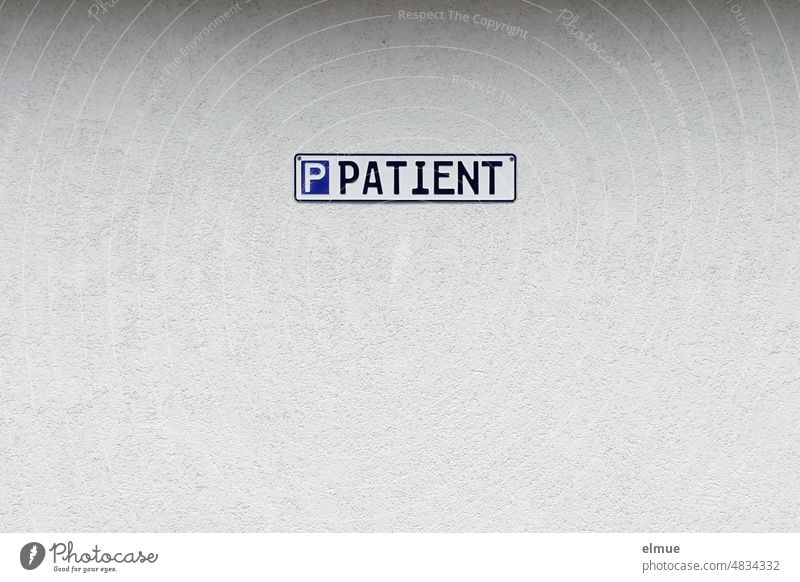 Ein Schild in Form eines Autokennzeichenschildes mit der Aufschrift  P Patient  an einer grau verputzten Wand / Parkplatz Patientenparkplatz parken reserviert