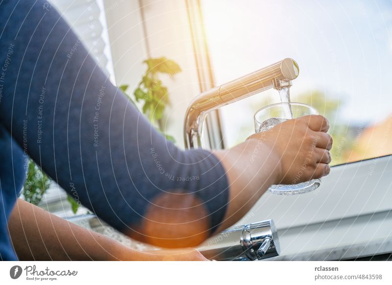 eine junge Frau, die sich in der Küche vor dem Fenster ein Glas sauberes Leitungswasser holt Wasser Wasserhahn trinken Brotbelag Waschbecken Lifestyle Hand