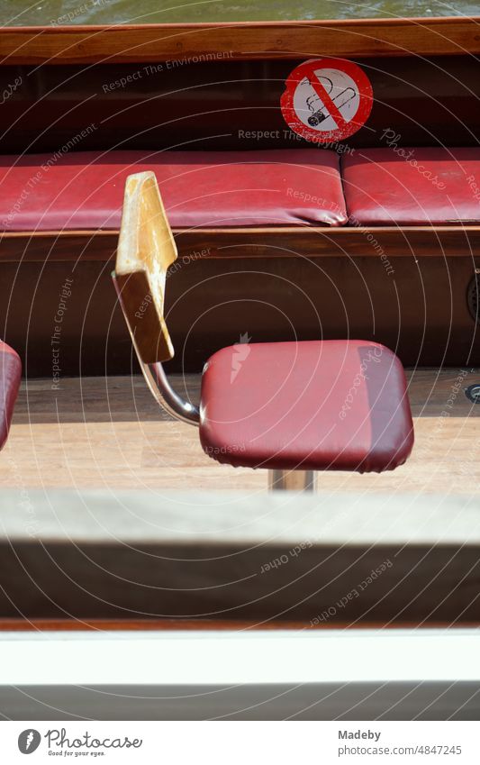Einzelner Sitz und rote Sitzbank auf einem Ausflugsboot bei Sonnenschein für Rundfahrten auf den Grachten in der Altstadt von Brügge in Westflandern in Belgien
