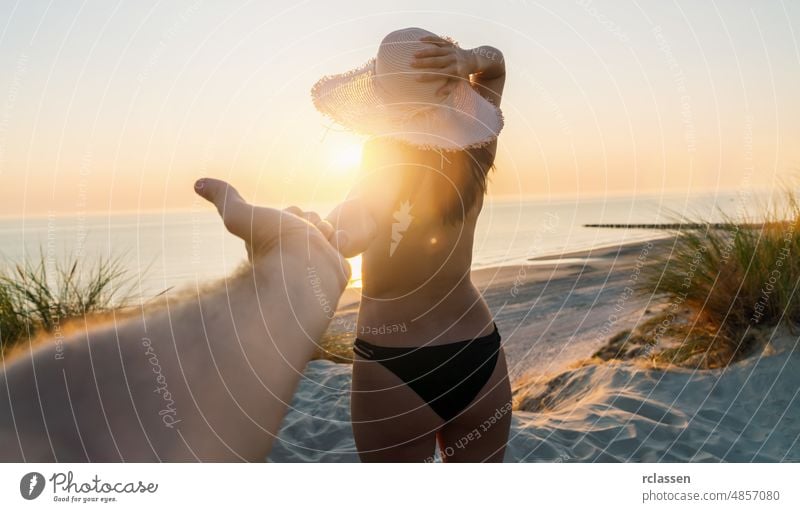 Paar, das sich an den Händen hält und bei Sonnenuntergang zum Strand geht, Frau mit Strohhut und Strandkleid - Ich-Perspektive Hand Person erste Sommer