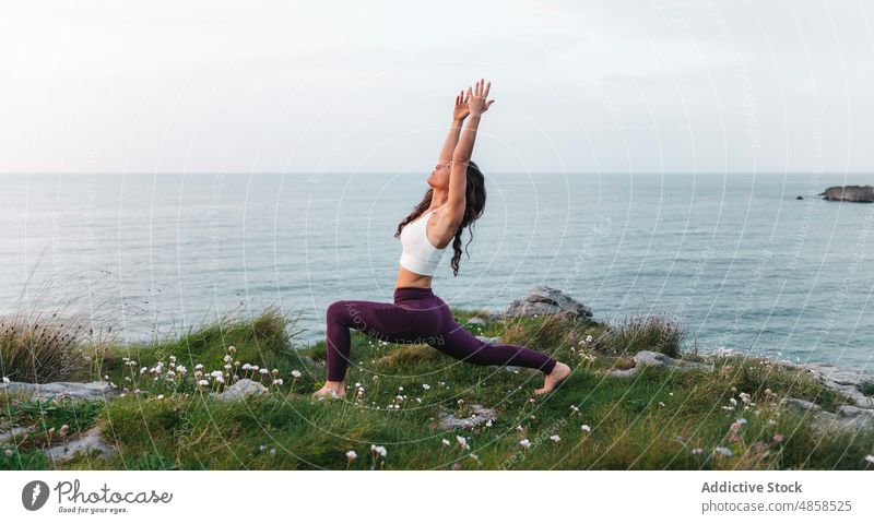 Sportliche Dame in Virabhadrasana-Pose beim Üben von Yoga am Meer Frau Krieger-Pose virabhadrasana MEER Dehnung Seeküste Asana Achtsamkeit beweglich Wellness