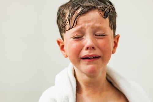 Trauriger Junge mit Tränen im Gesicht, eingewickelt in ein weißes Handtuch traurig verärgert Kind Augen geschlossen nasses Haar weinen Porträt Problematik