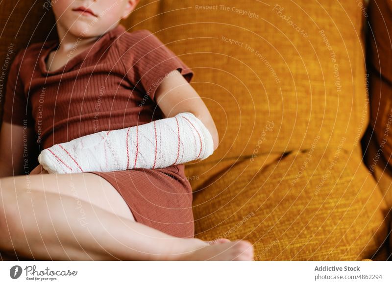 Anonymer süßer Junge mit gebrochenem Arm auf der Couch ruhen Sofa heimwärts Verletzung Wochenende Arme Wohnzimmer bandagieren verputzen Kind niedlich