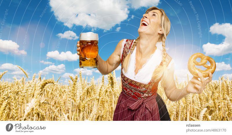 sexy traditioneller Oktoberfestbesucher, der in einem Weizenfeld steht, eine traditionelle bayerische Tracht trägt und einen großen Bierkrug und eine Brezel hält, im Herbst in Deutschland