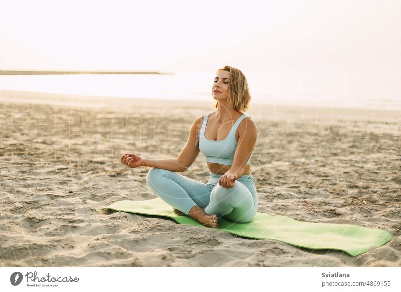 Eine glückliche junge Frau sitzt im Lotussitz und macht Yoga am Strand bei Sonnenuntergang. Das Konzept eines gesunden, aktiven Lebensstils Lotos MEER