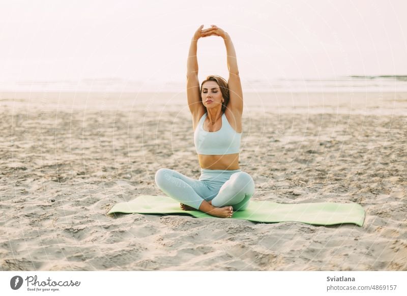 Ein attraktives Mädchen sitzt im Lotussitz und macht Übungen am Strand bei Sonnenuntergang. Das Konzept eines gesunden, aktiven Lebensstils Yoga Frau Lotos MEER