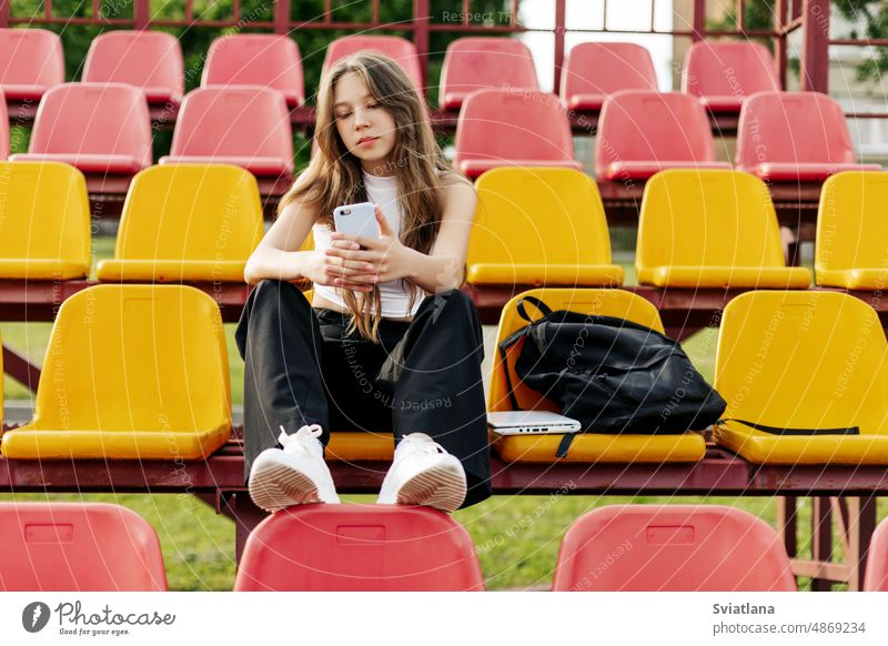Ein junges Mädchen sitzt auf der Tribüne der Schule und schreibt in ihrer Freizeit eine Nachricht auf ihrem Handy Telefon Schulmädchen tagsüber Smartphone