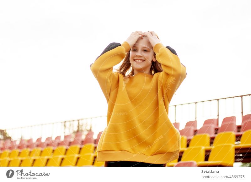 Ein lächelndes Teenager-Mädchen auf dem Hintergrund der Tribüne des Schulstadions Schule Stadion Schüler studierend Universität Gymnasium aussruhen nah jung