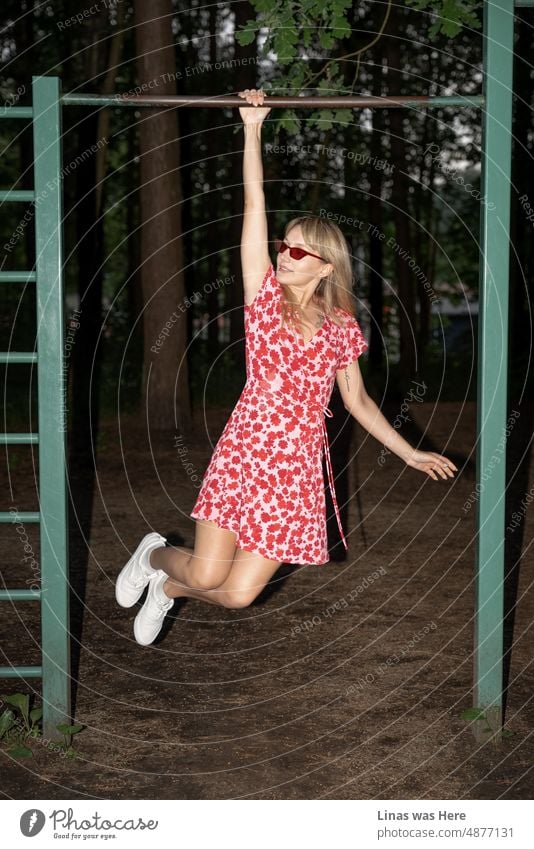 Ein starkes und schönes Mädchen in einem roten Kleid hat Spaß im Wald. Mit ihrer modischen Sonnenbrille und ihren weißen Turnschuhen ist sie ganz sicher die Königin des Waldes. Sommernächte mit etwas wilder Action.