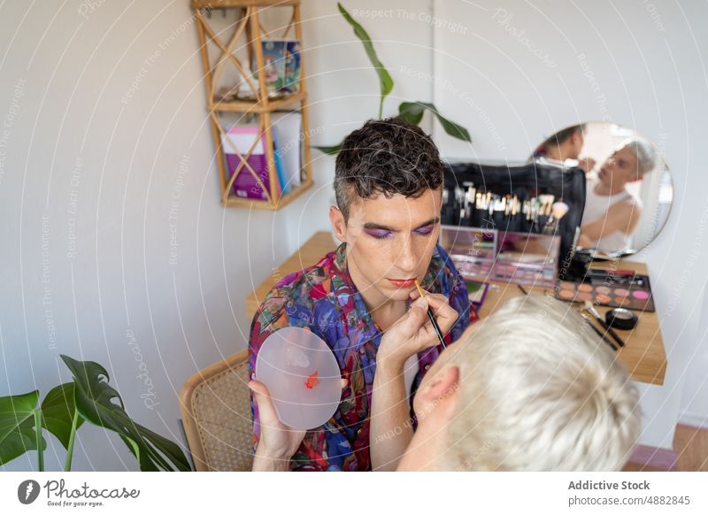 Androgyner Mann, der von seinem Freund am Tisch geschminkt wird Transgender Paar anwendend Lippenstift Künstler Kosmetik schwul Make-up Waschtisch rot