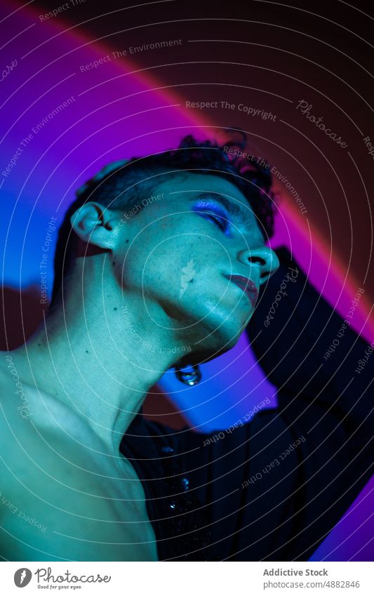 Transgender mit Lidschatten posiert auf beleuchtetem Hintergrund schwul Augen geschlossen posierend Make-up queer Mode Individualität lgbtqi Stolz