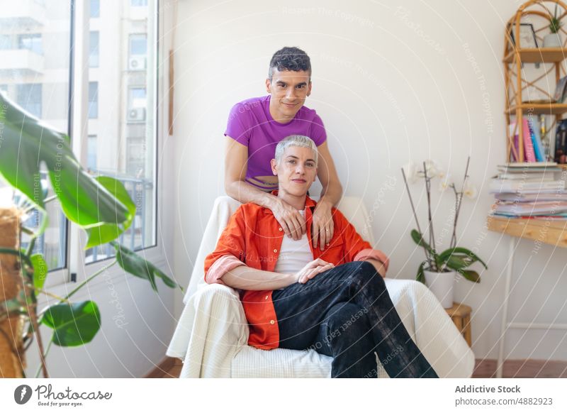 Lächelndes homosexuelles Paar, das auf einem Sessel zu Hause sitzt schwul Liebe Armsessel Umarmen Arm um Make-up Mode Glück Porträt Zusammensein Bonden queer