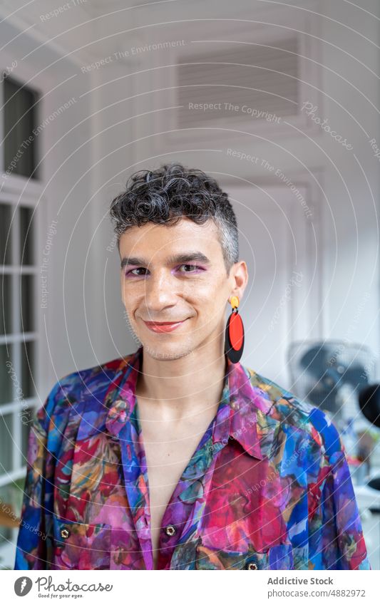 Selbstbewusster Transgender-Mann in lässigem Sitzen auf dem Sideboard Porträt schwul selbstbewusst Lifestyle Anrichte heimwärts Hemd Glück Ohrringe androgyn