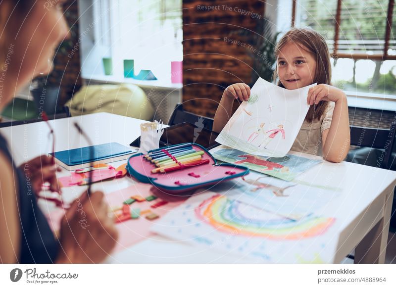 Mädchen präsentiert ihr Kunstwerk Lehrer. Frau unterstützt Schülerin während des Unterrichts in der Grundschule. Kind zeichnet Bild am Schreibtisch sitzend im Klassenzimmer. Lernen in der Grundschule. Zurück zur Schule