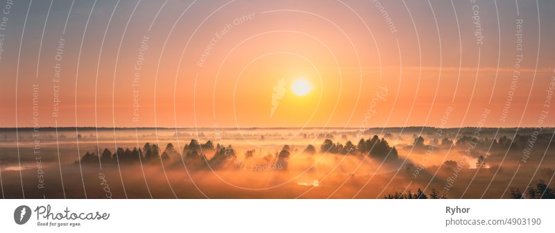 Amazing Sonnenaufgang Sonnenuntergang über neblige Landschaft. Scenic View Of Foggy Morning Sky With Rising Sun Above Misty Forest And River. Frühsommer Natur Osteuropas. Panorama