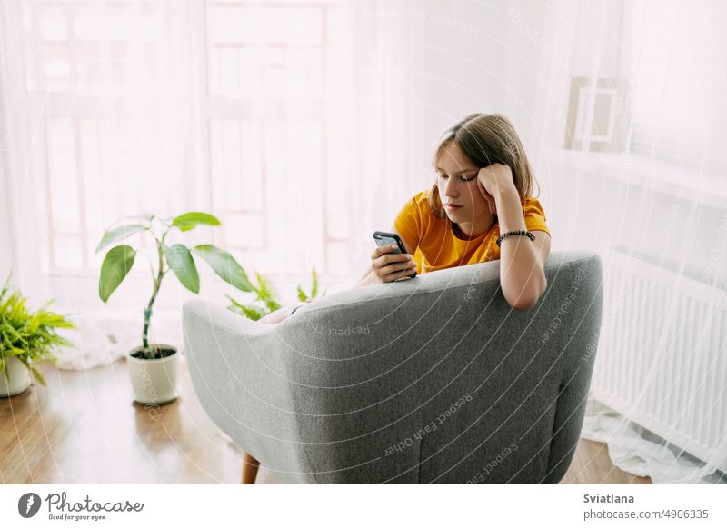 Ein junges Mädchen sitzt auf einem Stuhl und tauscht online Nachrichten über ihr Telefon aus. Freizeit zu Hause, moderner Lebensstil Schüler Sitzen