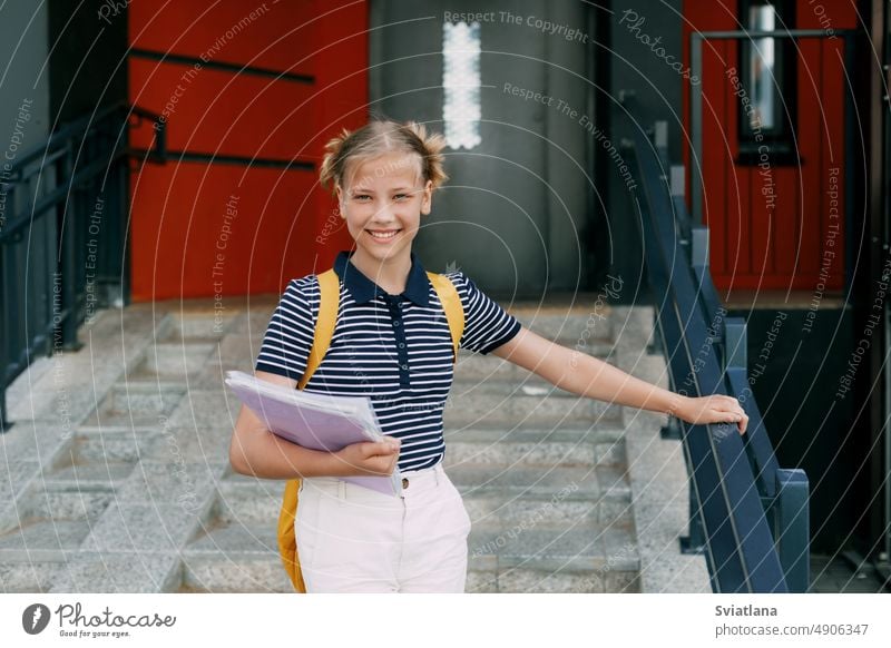 Ein lächelndes Teenager-Mädchen mit einem Rucksack und einem Ordner in der Hand geht die Treppe hinunter und eilt zur Schule. Zurück zur Schule, High School