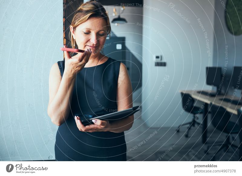 Geschäftsfrau mit Geschäftsanruf arbeiten auf Tablet im Büro. Reife beschäftigte Frau mit Touchpad-Computer stehend am Fenster in modernem Interieur Smartphone