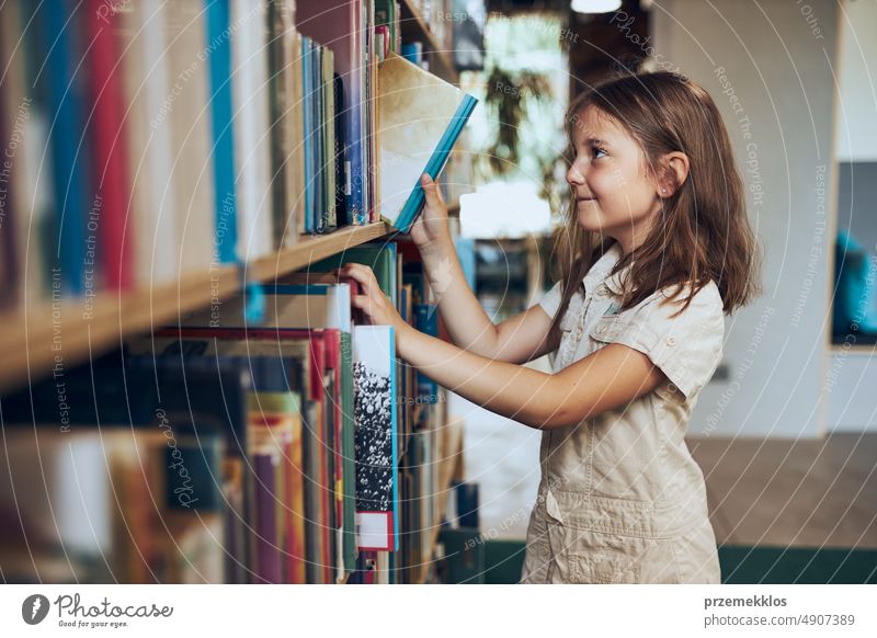 Schulmädchen wählt Buch in Schulbibliothek. Kluges Mädchen wählt Literatur zum Lesen aus. Aus Büchern lernen. Vorteile des täglichen Lesens. Kindliche Neugierde. Zurück zur Schule