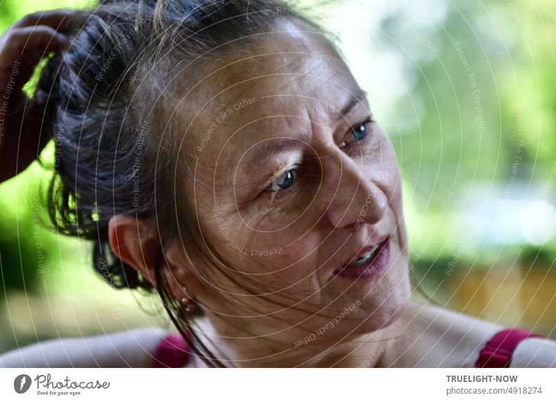 Frau. sommerlich ausdrucksstark im Halbprofil mit Blick in die Ferne, nackten Schultern mit roten Trägern und noch nassen Haaren am Ufer nach dem Schwimmen im Fluss