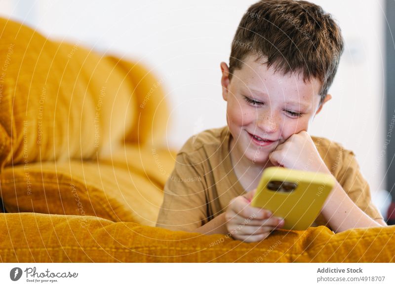 Glücklicher Junge auf einem Sofa liegend, der auf seinem Smartphone surft Kind heimwärts Telefon Browsen Lächeln Freude Technik & Technologie im Innenbereich